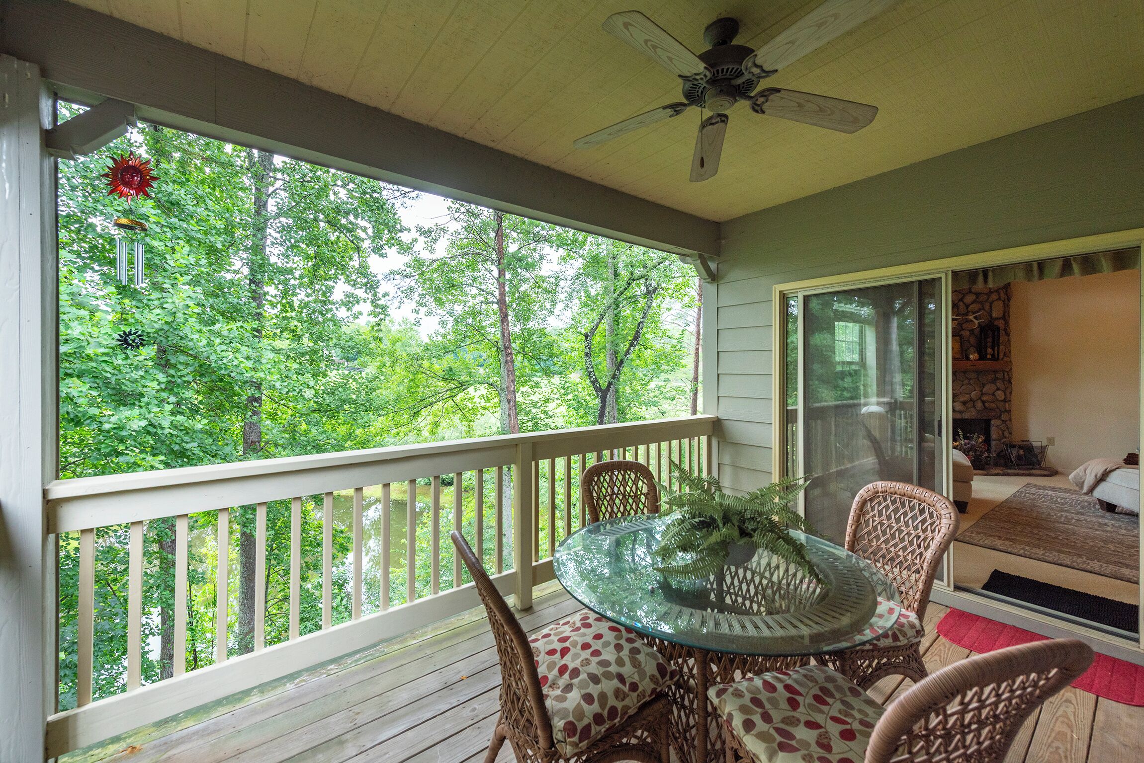 A covered porch with a table and chairs, a ceiling fan, and a view of a wooded area.