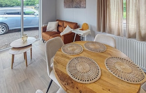 Een eetgedeelte met een houten tafel en geweven placemats, een bruine bank en een witte bijzettafel met een lamp.