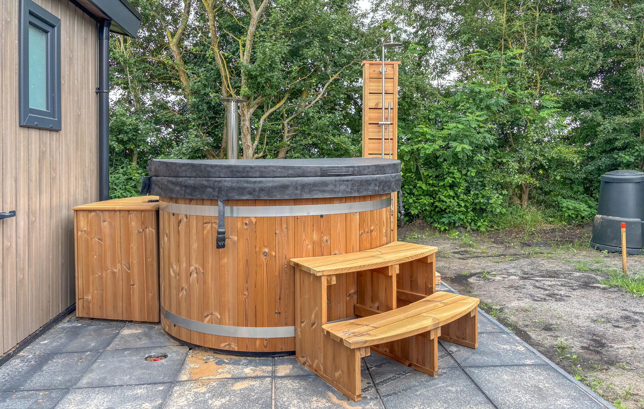 Un bain à remous en bois, doté d’un banc et d’une marche, entouré d’une clôture en bois et d’arbres.