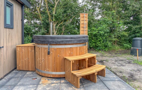 A wooden hot tub with a bench and a step, surrounded by a wooden fence and trees.