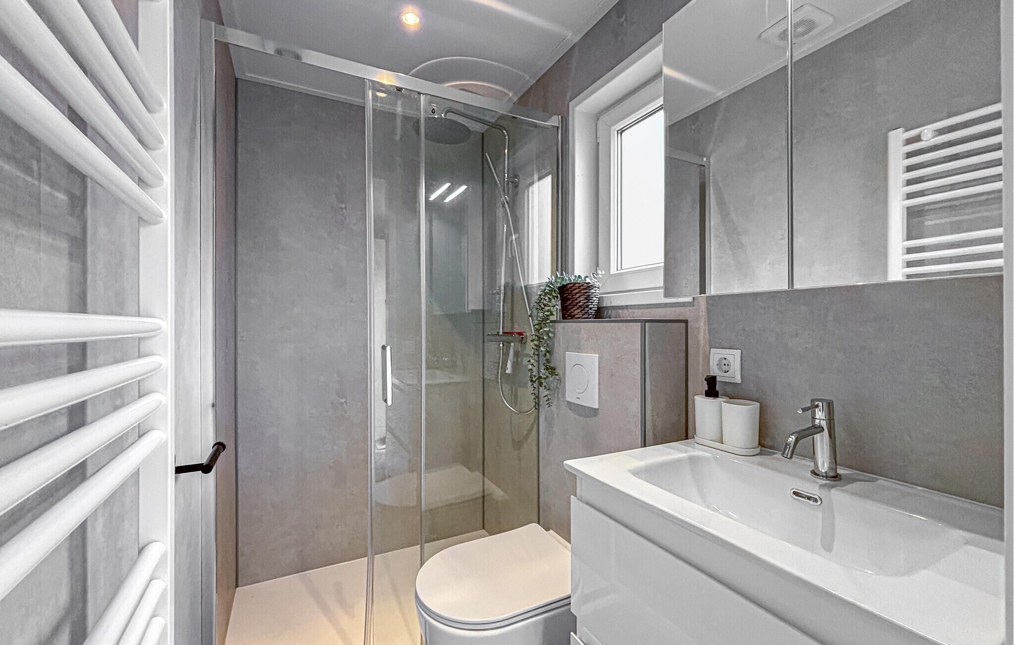 Une salle de bain moderne avec une douche à parois de verre, des toilettes blanches et un grand lavabo agrémenté d’un miroir.