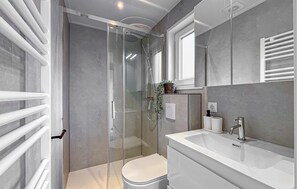 A modern bathroom with a glass-enclosed shower, a white toilet, and a large sink with a mirror.
