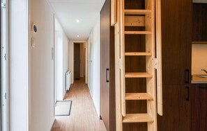 Un pasillo con una escalera de madera, un radiador y una puerta que da a otra habitación.