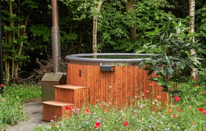 Un jacuzzi con escalones de madera y estructura metálica, rodeado por un jardín con diversas flores y árboles.