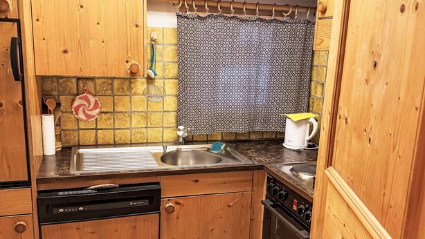 Cocina compacta con armarios de madera, lavavajillas, estufa y pileta.