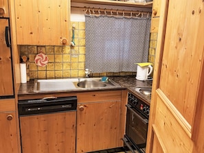 A compact kitchen with wooden cabinets, a dishwasher, a stove, and a sink. - Muntanella Nuov by Interhome (Sils Maria)