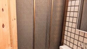 Un baño con puerta de madera, ducha con pared texturizada, pared azulejada y inodoro con tanque blanco.