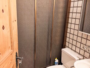 Ein Badezimmer mit Holztür, einer Dusche mit strukturierter Wand, einer Kachelwand und einem WC mit weißem Tank.