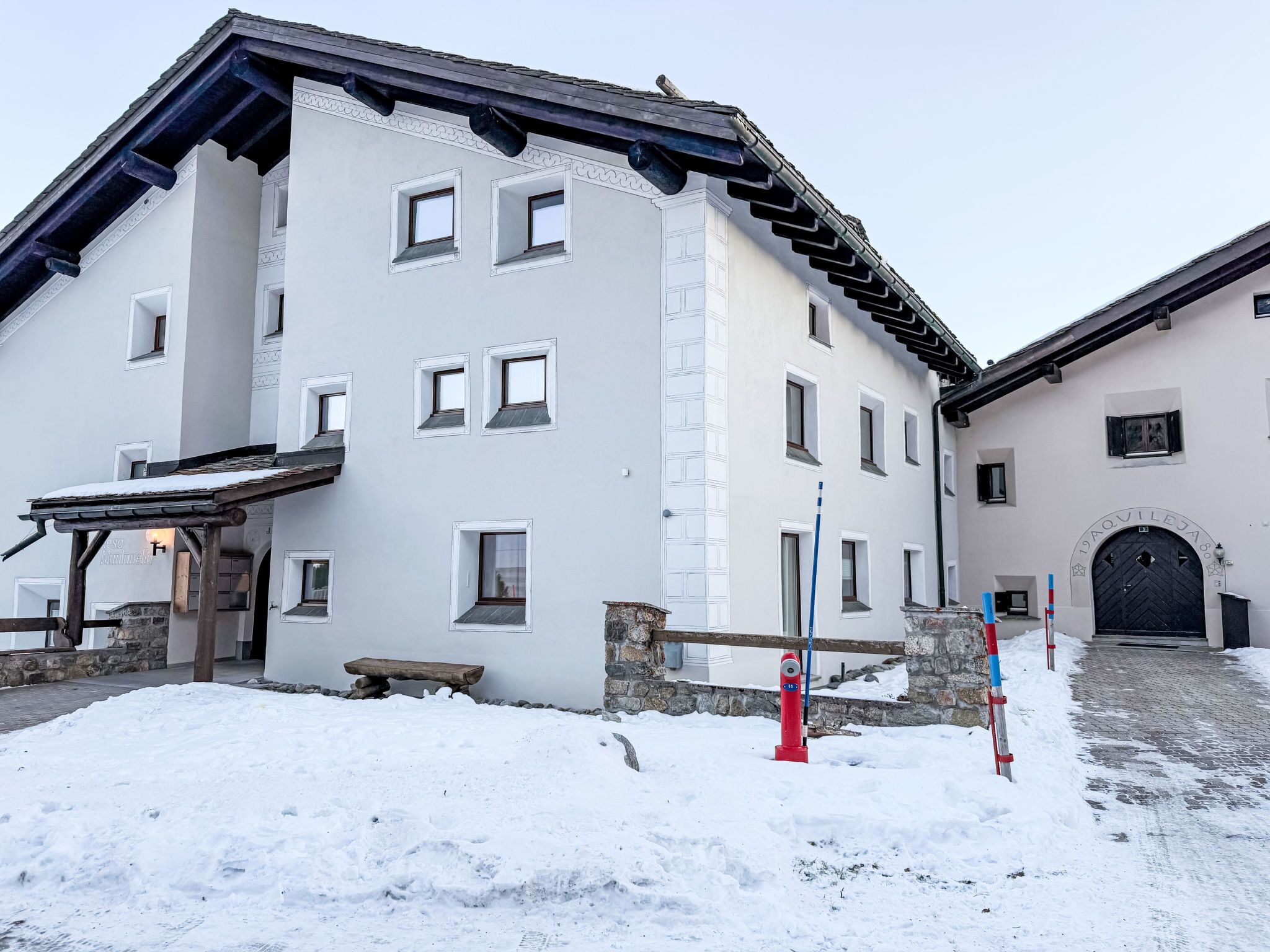 Um edifício de dois andares com várias janelas, uma parede de pedra e o chão coberto de neve.