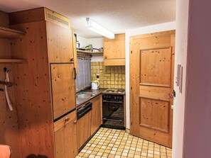 A compact kitchen with wooden cabinets, a stove, and a tiled backsplash. - Muntanella Nuov by Interhome (Sils Maria)