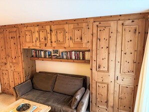 Ein gemütliches Zimmer mit einem Holzschrank, einem Bücherregal mit Büchern und einem braunen Ledersofa.