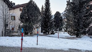 Un espacio exterior nevado con un camino pavimentado, árboles y un edificio al fondo.