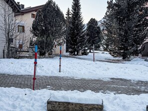 Eine verschneite Außenanlage mit einem gepflasterten Weg, Bäumen und einem Gebäude im Hintergrund.