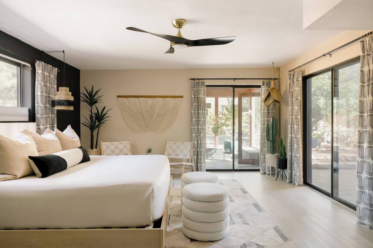 A modern bedroom with a large bed, a ceiling fan, and a view of the outdoors through a sliding glass door.