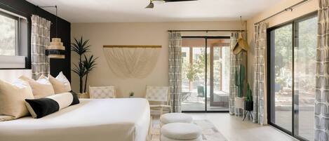 Une chambre moderne avec un grand lit, un ventilateur de plafond et une vue sur l’extérieur grâce à une porte-fenêtre coulissante.