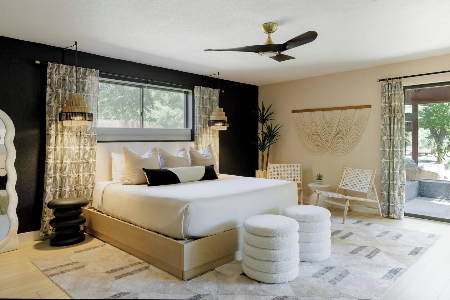 A modern bedroom with a bed, bedside lamps, a ceiling fan, and a view of the outdoors.