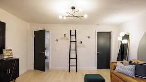 A room with a wooden floor, a black ladder, a sofa with cushions, a black cabinet, and a wall-mounted mirror. - ᔦ-𐌊𐌉𐌍Ᏽ 𐌄𐌍-𐌔𐌵𐌉𐌕𐌄𐌔 + 𝓗Ꝋ𐌕 𐌕𐌵𐌁 (Sedona)