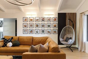 A living room with a brown sofa, a hanging chair, and a wall decorated with framed pictures. - Luxe Couples Retreat—Indoor Spa * 4 King En-Suites (Sedona)
