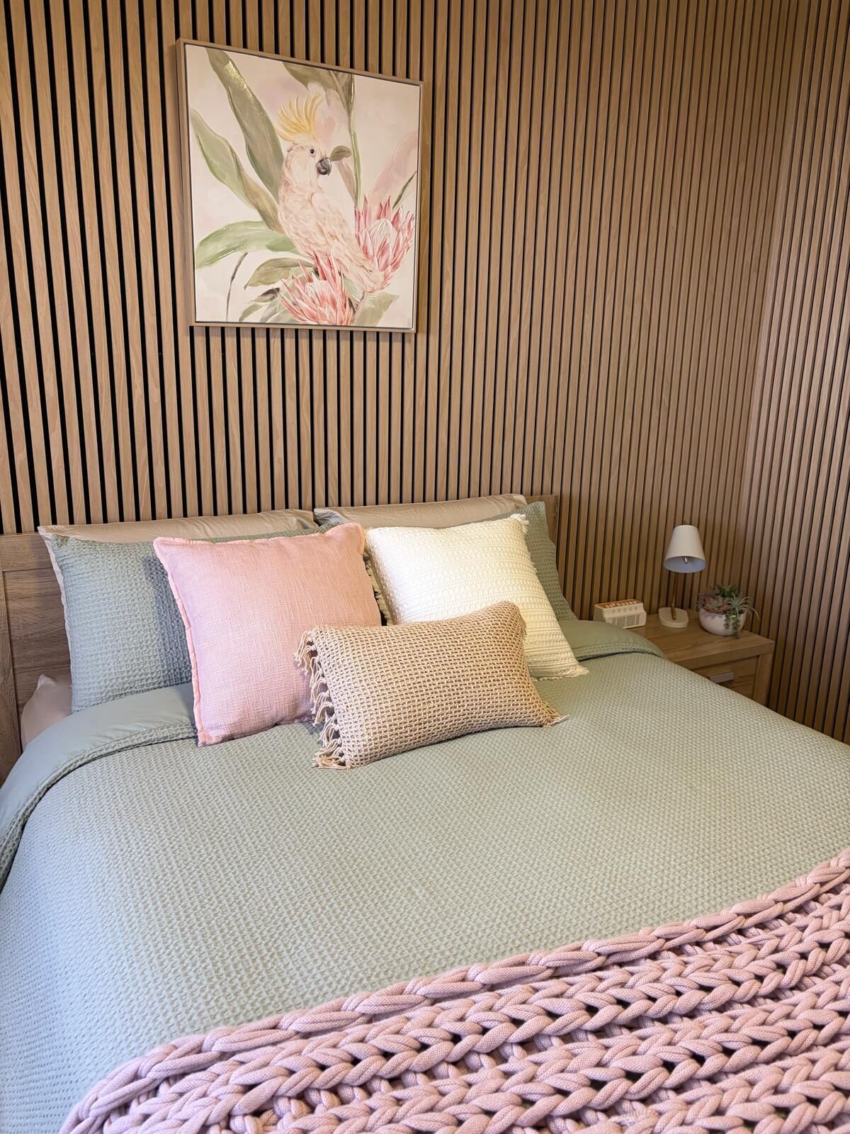 A bed with a textured green bedspread, multiple pillows, and a knitted throw.