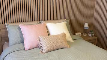 A bed with a textured green bedspread, multiple pillows, and a knitted throw.