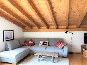 A modern living room with a grey sofa, wooden beams on the ceiling, a framed picture on the wall, and a floor lamp. - Mira Selva, (Flims Dorf), by Interhome (Flims)
