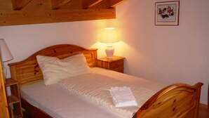A wooden bed with a white mattress and pillows, a bedside table with a lamp, and a framed picture on the wall. - Mira Selva, (Flims Dorf), by Interhome (Flims)
