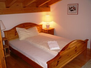 A wooden bed with a white mattress and pillows, a bedside table with a lamp, and a framed picture on the wall. - Mira Selva, (Flims Dorf), by Interhome (Flims)