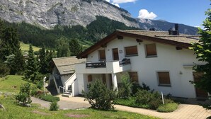 A two-story building with a balcony, surrounded by greenery and a mountainous backdrop. - Mira Selva, (Flims Dorf), by Interhome (Flims)