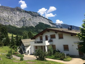 A two-story building with a balcony, surrounded by greenery and a mountainous backdrop. - Mira Selva, (Flims Dorf), by Interhome (Flims)