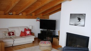A living room with a sofa, television, fireplace, and a ski-themed pillow. - Mira Selva, (Flims Dorf), by Interhome (Flims)