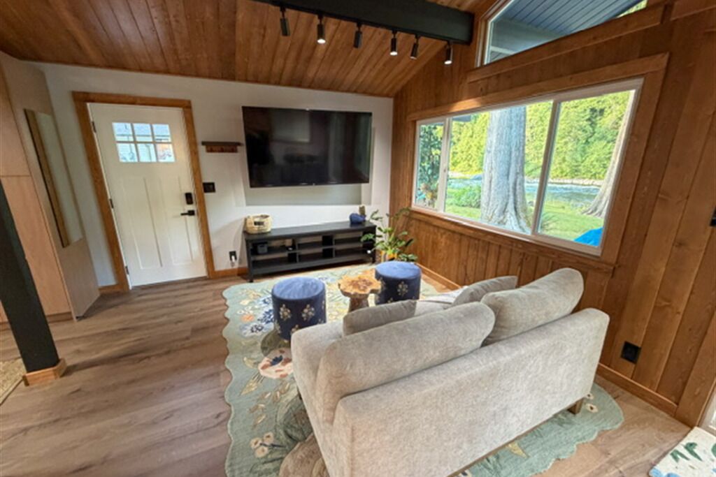 Een gezellige woonkamer met een bank, een flatscreen televisie en een raam met uitzicht op bomen.