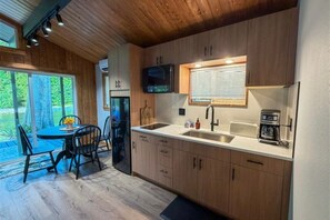 A modern kitchen with wooden cabinets, a built-in microwave, and a window with blinds.