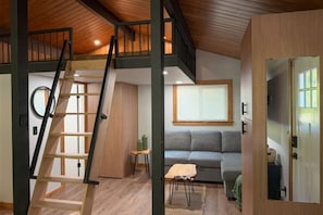 Una habitación estilo loft con escalera de madera, un sofá gris y una pequeña mesa.