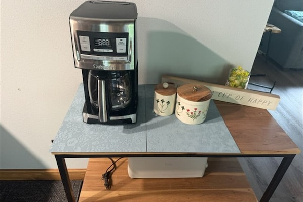 A coffee maker on a table with two decorative containers and a sign that reads 'Cup of Happy.'