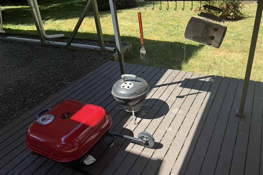 A barbecue grill on a wooden deck with a red grill cover and a gas tank.