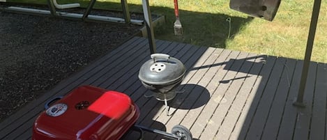 A barbecue grill on a wooden deck with a red grill cover and a gas tank.