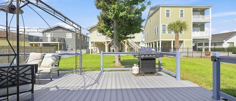 Un terrazzo in legno con altalena, barbecue e un albero sullo sfondo.