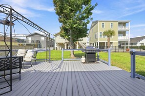 Eine Holzterrasse mit Schaukel, Grill und einem Baum im Hintergrund.