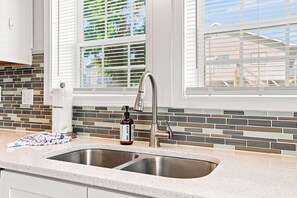 A kitchen with a double sink, a stainless steel faucet, and a soap dispenser on the countertop. - Sea La Vie | Coastal Comfort by the Beach (North Myrtle Beach)