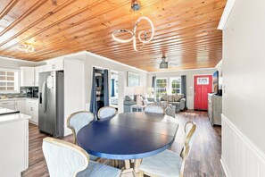 A modern kitchen with stainless steel appliances, a dining area with a round table and chairs, and a red door. - Sea La Vie | Coastal Comfort by the Beach (North Myrtle Beach)
