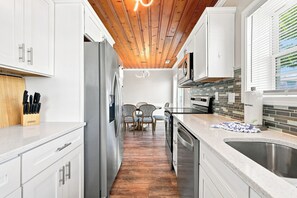 A modern kitchen with white cabinetry, stainless steel appliances, and a wooden ceiling. - Sea La Vie | Coastal Comfort by the Beach (North Myrtle Beach)