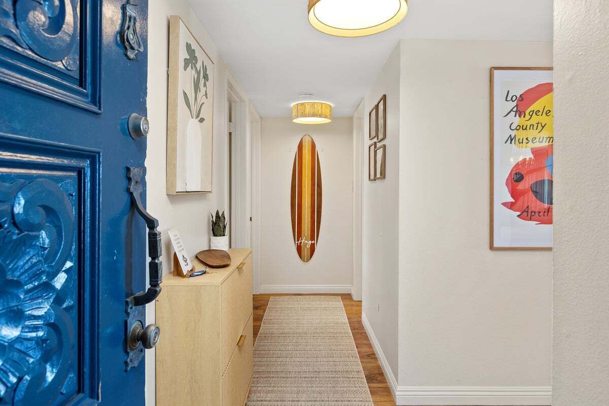 Um corredor com porta azul, um armário de madeira, um enfeite de prancha de surf e uma placa emoldurada do Museu do Condado de Los Angeles.