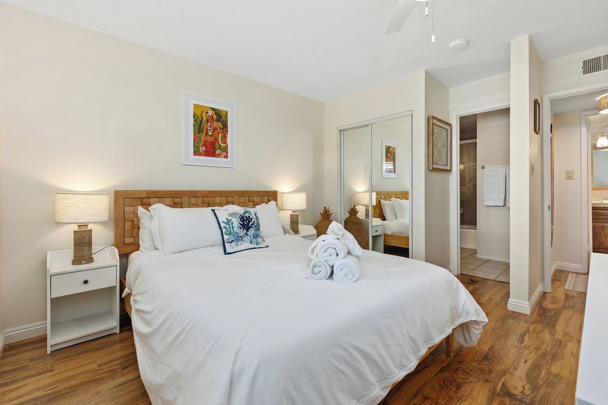 A hotel room with a large bed, a nightstand, a bedside table, a mirror, and a door leading to a bathroom.