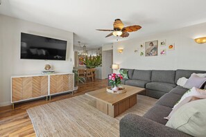 A modern living room with a grey sofa, a wooden coffee table, and a ceiling fan. - TRUE Oceanfront • Steps to Beach • Pool 205A (Oceanside)