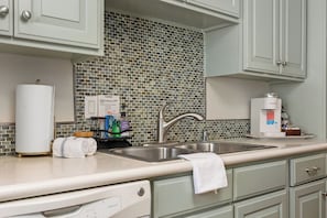 A kitchen with a tiled backsplash, a coffee machine, and a sink. - TRUE Oceanfront • Steps to Beach • Pool 205A (Oceanside)