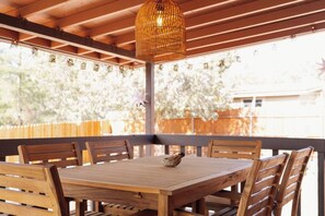 Ein Holztisch und Stühle im Freien unter einer Pergola mit einer gewebebespannten Leuchte.