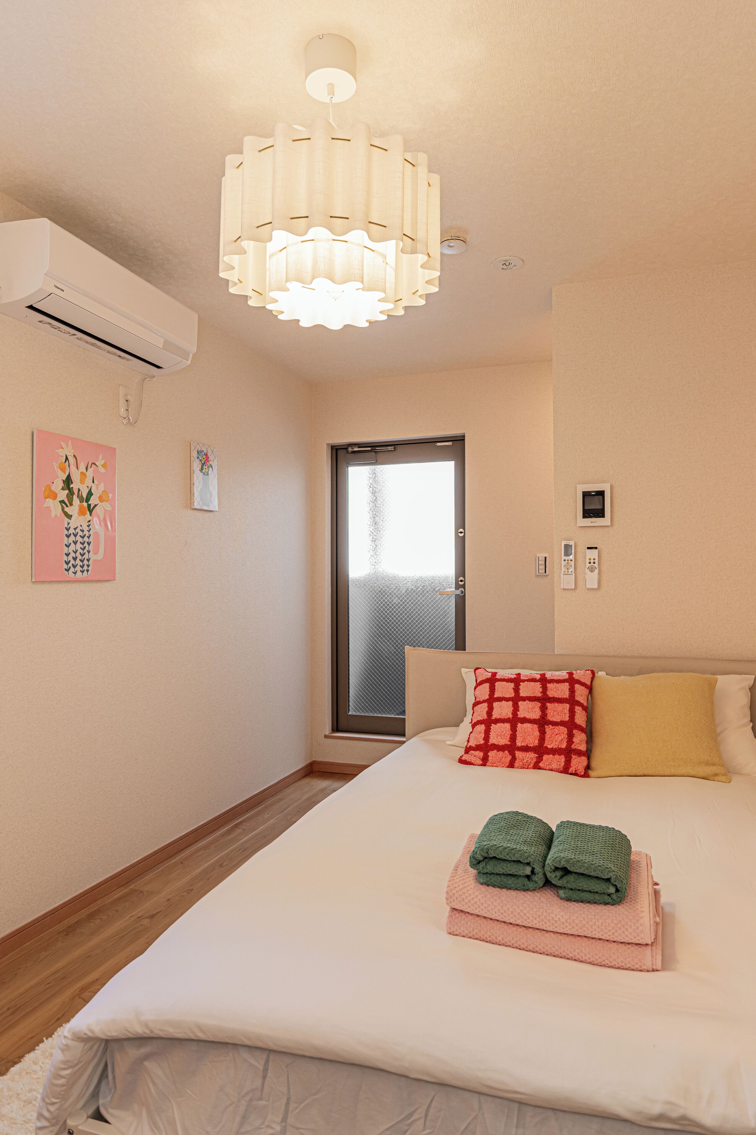 A hotel room with a bed, a door, an air conditioning unit, and a wall-mounted light fixture.