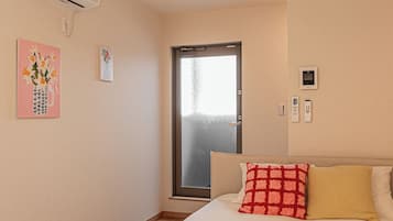 A hotel room with a bed, a door, an air conditioning unit, and a wall-mounted light fixture.