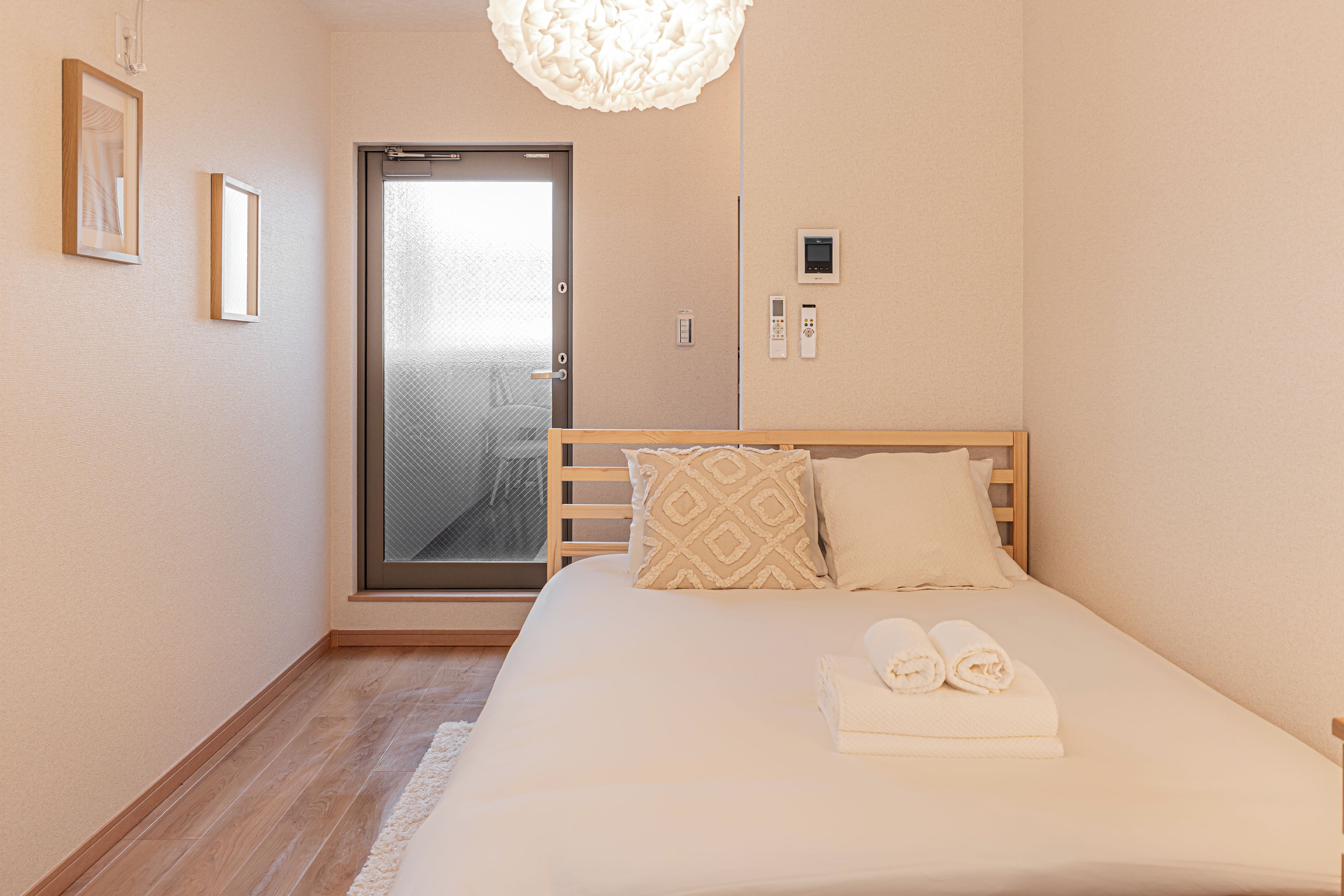 A hotel room with a bed, a door with a frosted glass panel, a wall-mounted control panel, and a light fixture.