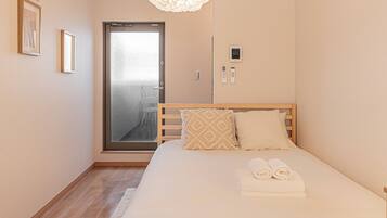 A hotel room with a bed, a door with a frosted glass panel, a wall-mounted control panel, and a light fixture.